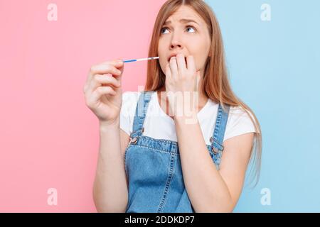 Sì, sono pregnantA scioccata bella giovane donna incinta mostra un risultato positivo di due strisce su un test, in piedi su un isolato rosa e blu backg Foto Stock