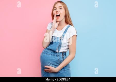 Una bella donna in stato di scioccato guarda la macchina fotografica e urla, tenendola in bocca, su uno sfondo rosa e blu Foto Stock