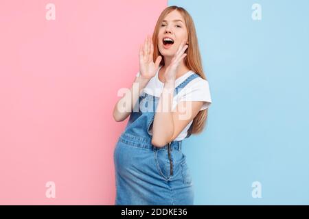 Una bella donna in stato di scioccato guarda la macchina fotografica e urla, tenendola in bocca, su uno sfondo rosa e blu Foto Stock