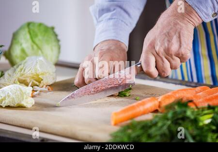 Vista tagliata di uomo maturo tagliando verdure fresche per insalata. Abitudini alimentari sane. Primo piano delle mani maschili. Preparazione degli alimenti. Foto Stock