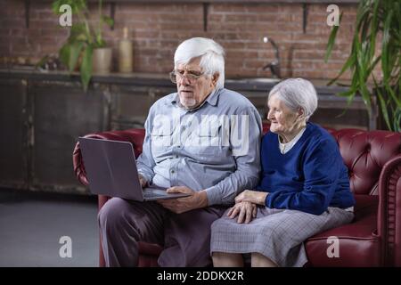 Uomo maturo e donna anziana che usa il computer portatile mentre si siede sul divano. Guardare video o navigare sul Web su un computer portatile. Foto Stock