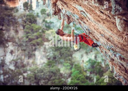 Scalatore di roccia che scalda la corda mentre si arrampica su un percorso impegnativo su una scogliera a strapiombo. Foto Stock