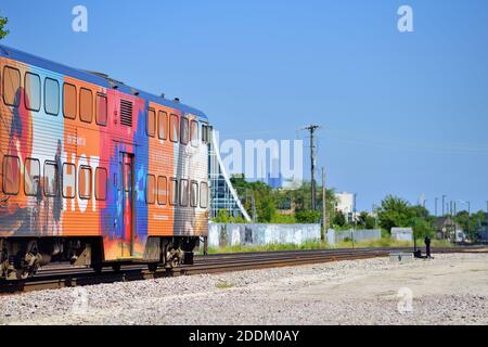 Chicago, Illinois, Stati Uniti. Un treno Metra in arrivo con un'auto di guida sportiva colorata pubblicità trasporta pendolari a Chicago. Foto Stock