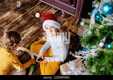 I bambini piccoli costruiscono la ferrovia e giocano con il treno giocattolo sotto l'albero di Natale. Bambini con regali di Natale. Tempo di Natale. Foto Stock