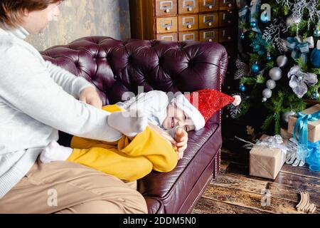 Felice caucasico papà tickle divertirsi con eccitato piccolo figlio preschooler a Santa Hat. Rilassati insieme, amando il padre che gioca con il ragazzino sorridente Foto Stock