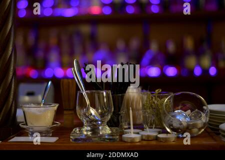 Serve oggetti sullo sfondo di luci viola della vetrina. Bancone bar con piatti, ciotola di zucchero, cucchiaini da tè, candele, paillette, spiedini, in un caffè Foto Stock