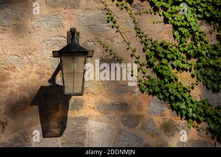 Vecchia lanterna forgiata d'epoca su un muro di pietra naturale coperto con edera Foto Stock