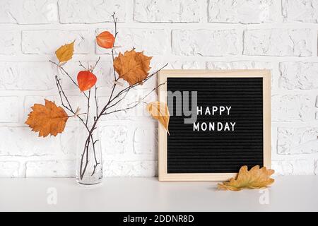 Happy Lunedi testo su bordo nero lettera e bouquet di rami con foglie gialle su clothespins in vaso sul tavolo modello per cartolina, auto di saluto Foto Stock