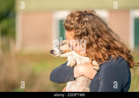 Coltivatore e il suo amore per gli animali domestici. Jack Russell Terrier cane giace nelle braccia womans. Stabile in background. Foto Stock