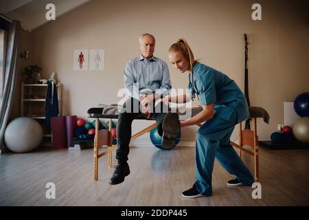 Anziano uomo in pensione facendo esercizi fisici con la giovane fisioterapista femminile in clinica Foto Stock