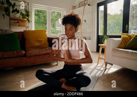 Giovane donna africana seduta in loto con mani unite su tappetino yoga esercizio di respirazione Foto Stock