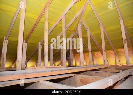 Una vista su sottotetto incompiuto dall'interno della casa con un primo piano su travetti in legno soffitto, travi del tetto, travi, borchie da parete e film barriera al vapore inst Foto Stock