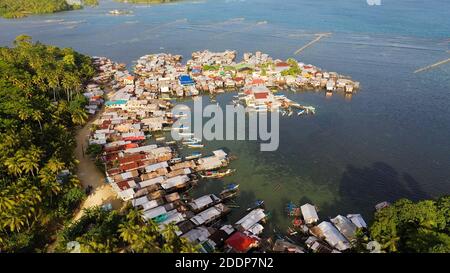 Una piccola barca Outrigger ormeggiata vicino a una casa su palafitte in un villaggio di pescatori. Villaggio costiero di pescatori. Filippine, Mindanao. Foto Stock