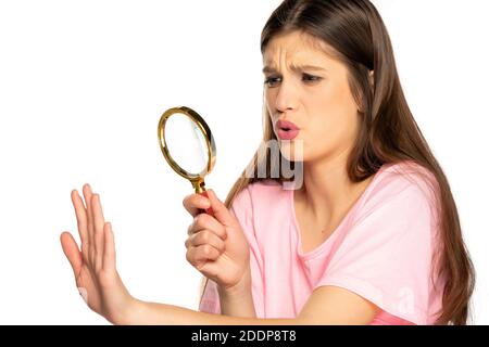 Giovane donna preoccupata che guarda le unghie con lente d'ingrandimento sopra sfondo bianco Foto Stock