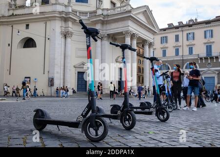 Scooters elettrici Dott parcheggiato in Piazza del Popolo allineato e pronto per l'affitto. In background alcuni ragazzi li affittano utilizzando l'app RideDott per Foto Stock