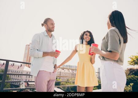 Foto di tre bellissimi compagni in piedi tenere a mano tazza di bevanda parlare godetevi una giornata di sole che si riunisce all'aperto Foto Stock