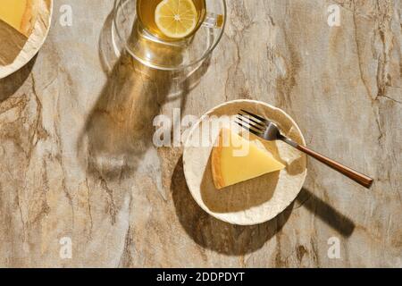 Vista dall'alto di un pezzo di torta al limone con tè sotto luce solare diretta con ombre dure sul tavolo Foto Stock