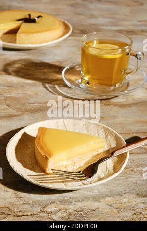 Pezzo di crostata di limone con tè sotto la luce diretta del sole con ombre dure sul tavolo Foto Stock