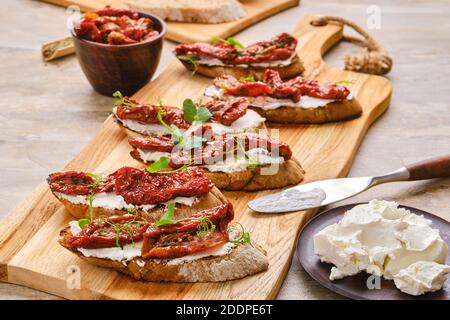 Tostatura con formaggio di capra e pomodoro essiccato su taglio di legno scheda Foto Stock