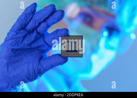 Un ingegnere che lavora in un laboratorio indossando una speciale uniforme e guanti protettivi detiene il nuovo processore in mani e lo esamina Foto Stock