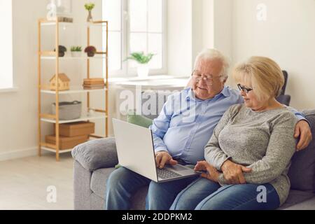 Uomo anziano e donna seduti sul divano nel soggiorno guardando il film sul computer portatile insieme. Foto Stock