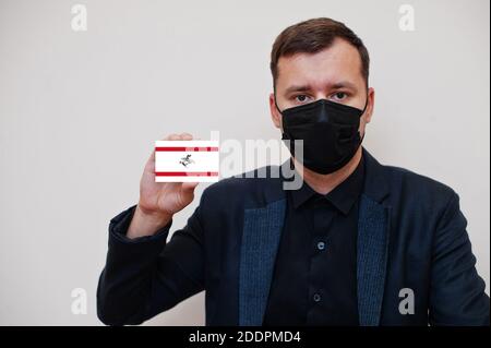 Uomo italiano indossare nero formale e proteggere maschera viso, tenere toscano carta bandiera isolato su sfondo bianco. Italia regioni coronavirus Covid Concept. Foto Stock