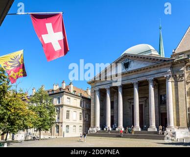 Facciata neoclassica della cattedrale di San Pietro nel centro storico di Ginevra con una bandiera svizzera e una bandiera di Ginevra appesa al cielo blu. Foto Stock