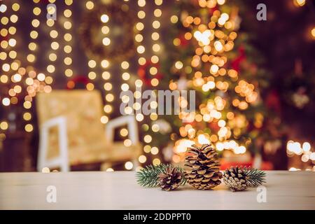 Fuoco selettivo sui coni di pino, soggiorno offuscato con albero di Natale decorato e sedia. Molte luci delle fate illuminate. Prodotti a tema natalizio Foto Stock