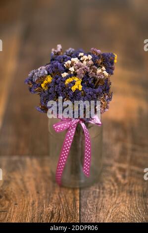 Un bouquet di fiori secchi, limonium sinusatum, lavanda di mare a foglia d'onda, statice, rosmarino a foglia di intaglio, rosa di mare in vaso, nastro rosa, pavimento in legno Foto Stock