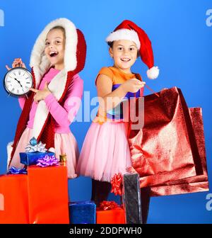 I ragazzi di Santa Claus cappelli aprire dono scatole e confezioni. Le ragazze aspettare per il nuovo anno puntando alla sveglia. Festeggiando e concetto di vacanza. I bambini con facce felici giocare su sfondo blu. Foto Stock