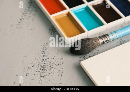 Album di schizzo bianco, pennello scoiattolo e vernici acquerello con spazio di copia, vista dall'alto, luce del giorno. Concetto di spazio di lavoro dell'artista Foto Stock