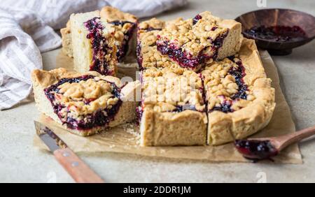 Torta di marmellata di frutti di bosco fatti in casa su carta da forno, fondo di cemento chiaro. Torta crumble. Foto Stock