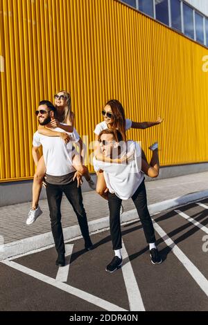 Un gruppo di amici ridere e camminare intorno al centro della città.si abbracciano e sorridono, i ragazzi portano le ragazze sulle loro spalle Foto Stock