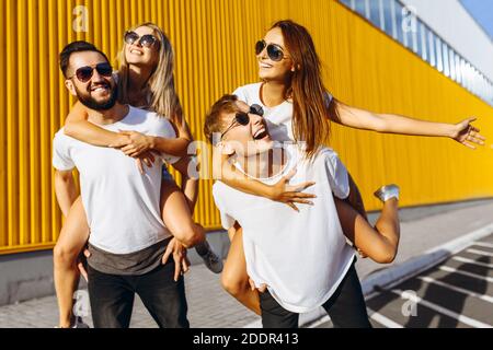 Un gruppo di amici ridere e camminare intorno al centro della città.si abbracciano e sorridono, i ragazzi portano le ragazze sulle loro spalle Foto Stock