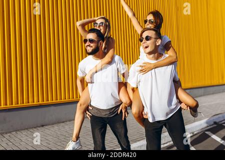 Un gruppo di amici ridere e camminare intorno al centro della città.si abbracciano e sorridono, i ragazzi portano le ragazze sulle loro spalle Foto Stock