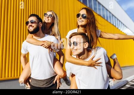 Un gruppo di amici ridere e camminare intorno al centro della città.si abbracciano e sorridono, i ragazzi portano le ragazze sulle loro spalle Foto Stock