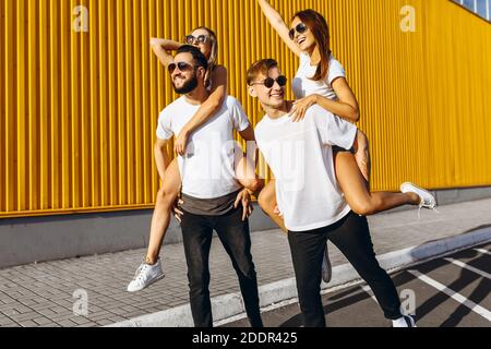 Un gruppo di amici ridere e camminare intorno al centro della città.si abbracciano e sorridono, i ragazzi portano le ragazze sulle loro spalle Foto Stock