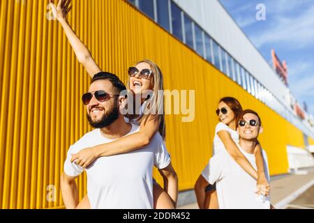 Un gruppo di amici ridere e camminare intorno al centro della città.si abbracciano e sorridono, i ragazzi portano le ragazze sulle loro spalle Foto Stock