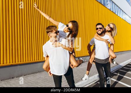 Un gruppo di amici ridere e camminare intorno al centro della città.si abbracciano e sorridono, i ragazzi portano le ragazze sulle loro spalle Foto Stock