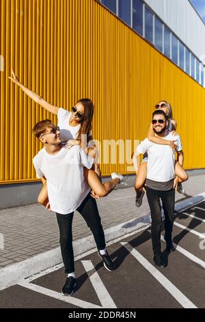 Un gruppo di amici ridere e camminare intorno al centro della città.si abbracciano e sorridono, i ragazzi portano le ragazze sulle loro spalle Foto Stock