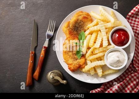 piatto di schnitzel di pollo e patatine fritte su sfondo scuro, vista dall'alto Foto Stock