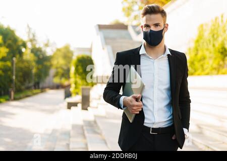 Bell'uomo d'affari biondo in maschera di faccia che posa con il laptop su via della città Foto Stock