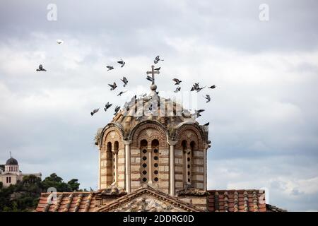 Gregge di piccioni che volano intorno alla cupola della chiesa greco-ortodossa nella zona di Thissio, Atene, Grecia. Edificio nazionale osservatorio e cielo nuvoloso backgro Foto Stock