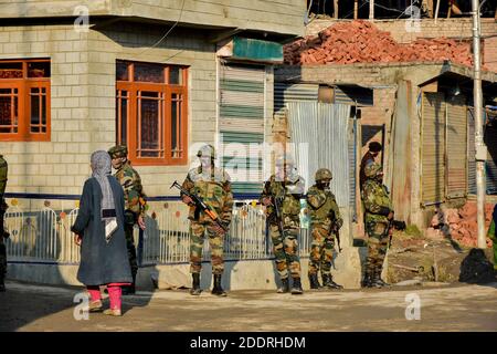 Una donna passa accanto ai soldati dell'esercito indiano in piedi allerta vicino al sito di un attacco a Srinagar, la capitale estiva di Jammu e Kashmir.due soldati dell'esercito indiano sono stati uccisi in un attacco militante alla periferia di Srinagar. I soldati facevano parte di una squadra di pattuglia dell'esercito che era stata sottoposta a forti sparazioni da parte dei militanti, ha detto la polizia. Foto Stock