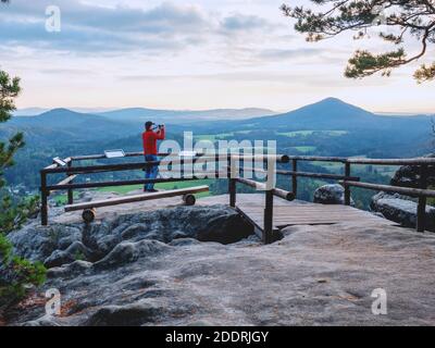 L'uomo sulla roccia scatta foto di paesaggi di montagna. Il viaggiatore prende il panorama mozzafiato delle montagne sulla macchina fotografica in mano Foto Stock