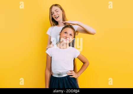 Felice mamma bella con la figlia piccola, mamma misura l'altezza di sua figlia mentre si trova su uno sfondo giallo Foto Stock