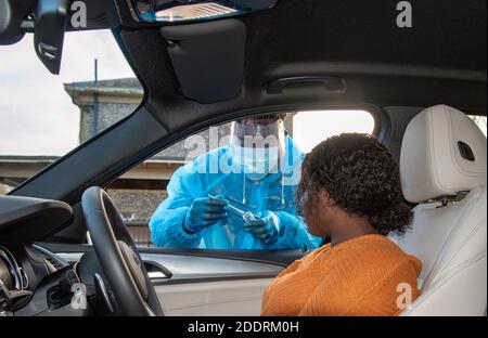 Inghilterra meridionale, Regno Unito. 2020. Cliente nero al centro di test Covid-19 con campione di siliva prelevato con un batuffolo di cotone da un tester femmina. Foto Stock