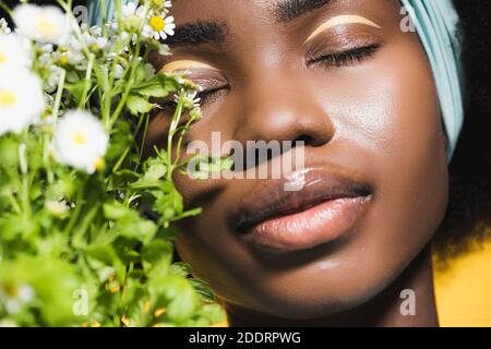 primo piano di giovane donna afro-americana con bouquet camomilla isolato giallo acceso Foto Stock
