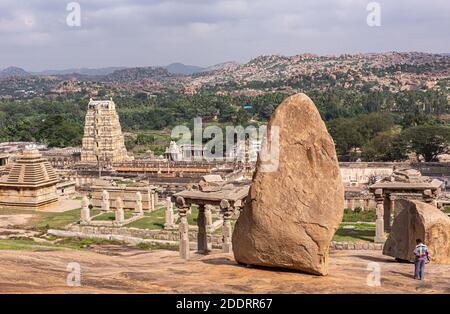 Hampi, Karnataka, India - 4 novembre 2013: Complesso del Tempio di Virupaksha. Ampia vista sui giardini del tempio con un gigantesco masso marrone sull'altopiano abov Foto Stock