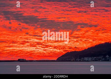 Charmouth, Dorset, Regno Unito. 26 novembre 2020. Uno spettacolare tramonto rosso fuoco sul porto di Cobb e Lyme Regis in Dorset vista dalla spiaggia di Charmouth alla fine di una giornata di sole Picture Credit: Graham Hunt/Alamy Live News Foto Stock